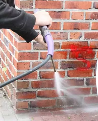 A Man Cleaning Graffiti Using High Water Pressure From Brick Wall Image